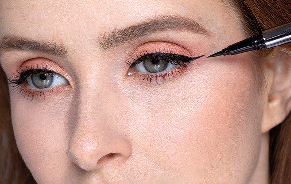 Woman applying black liquid eyeliner to create a winged eye makeup look.